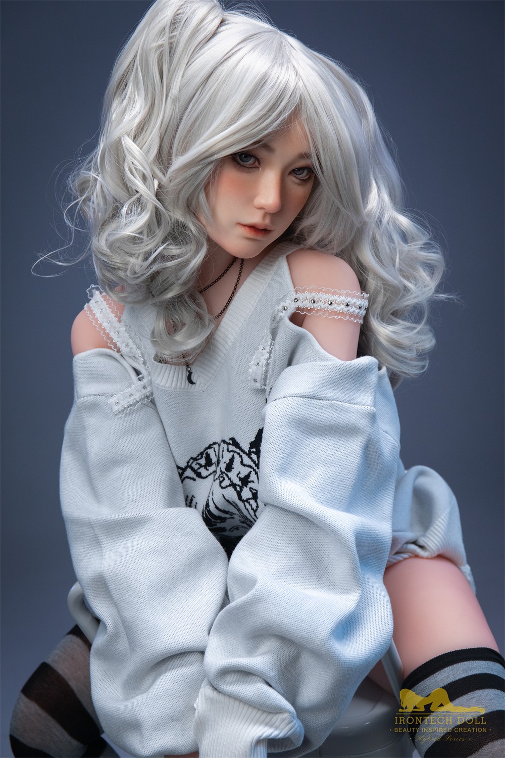 Olivia, a 154 cm hybrid sex doll, seated with silver curled hair and a printed sweater