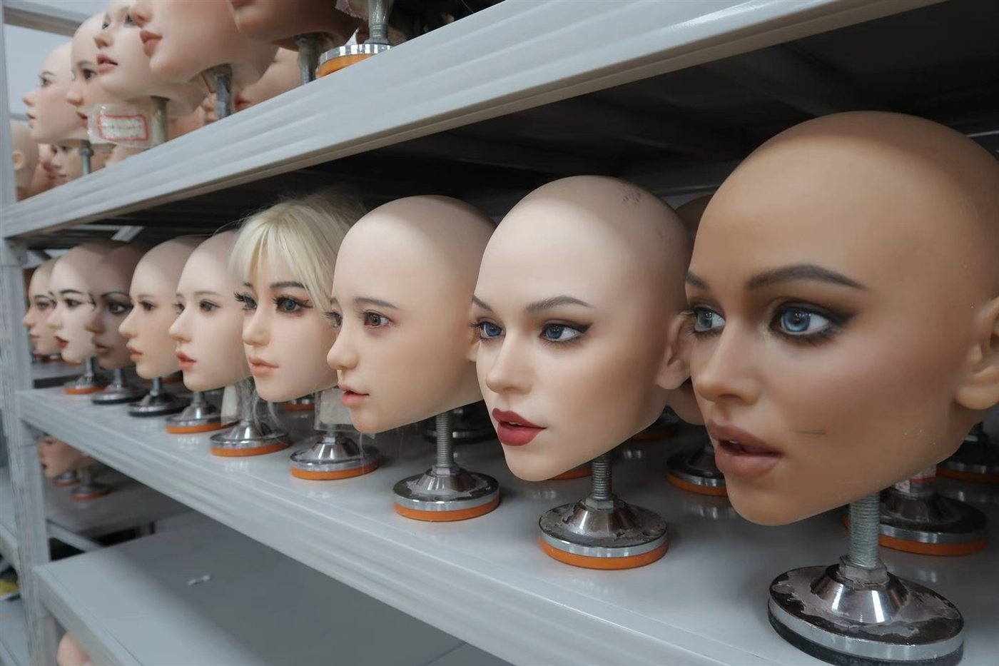 Painted sex doll head sculpts lined up on workshop shelves